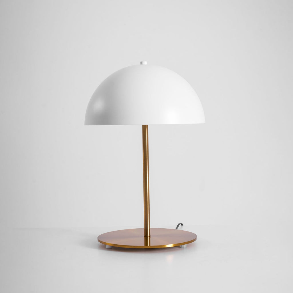 White dome table lamp from Clérachic seen from slightly above, with its round brass base and cord on a light backdrop.