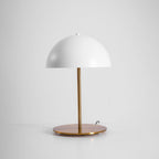 White dome table lamp from Clérachic seen from slightly above, with its round brass base and cord on a light backdrop.