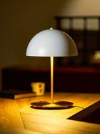 Warmly lit white dome table lamp from Clérachic casting a golden pool of light across a wooden desk in a dim room.