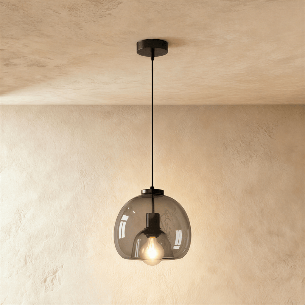 Clérachic single pendant with a smoked glass shade, a black cord and ceiling rose, its filament bulb lit against limewash.