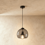 Clérachic single pendant with a smoked glass shade, a black cord and ceiling rose, its filament bulb lit against limewash.