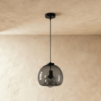 Clérachic single smoked glass pendant with matte black cord and canopy, shown unlit against a limewashed wall.
