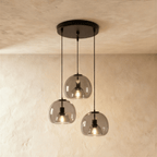 Clérachic three-light pendant cluster with smoked glass shades hanging at three heights from a round matte black canopy.
