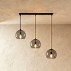 Clérachic three-light pendant with smoked glass shades at stepped heights from a slim linear matte black bar canopy.
