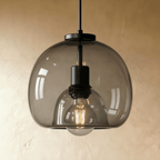 Close view of the Clérachic pendant's smoked glass shade, matte black fitting and warm filament bulb inside.