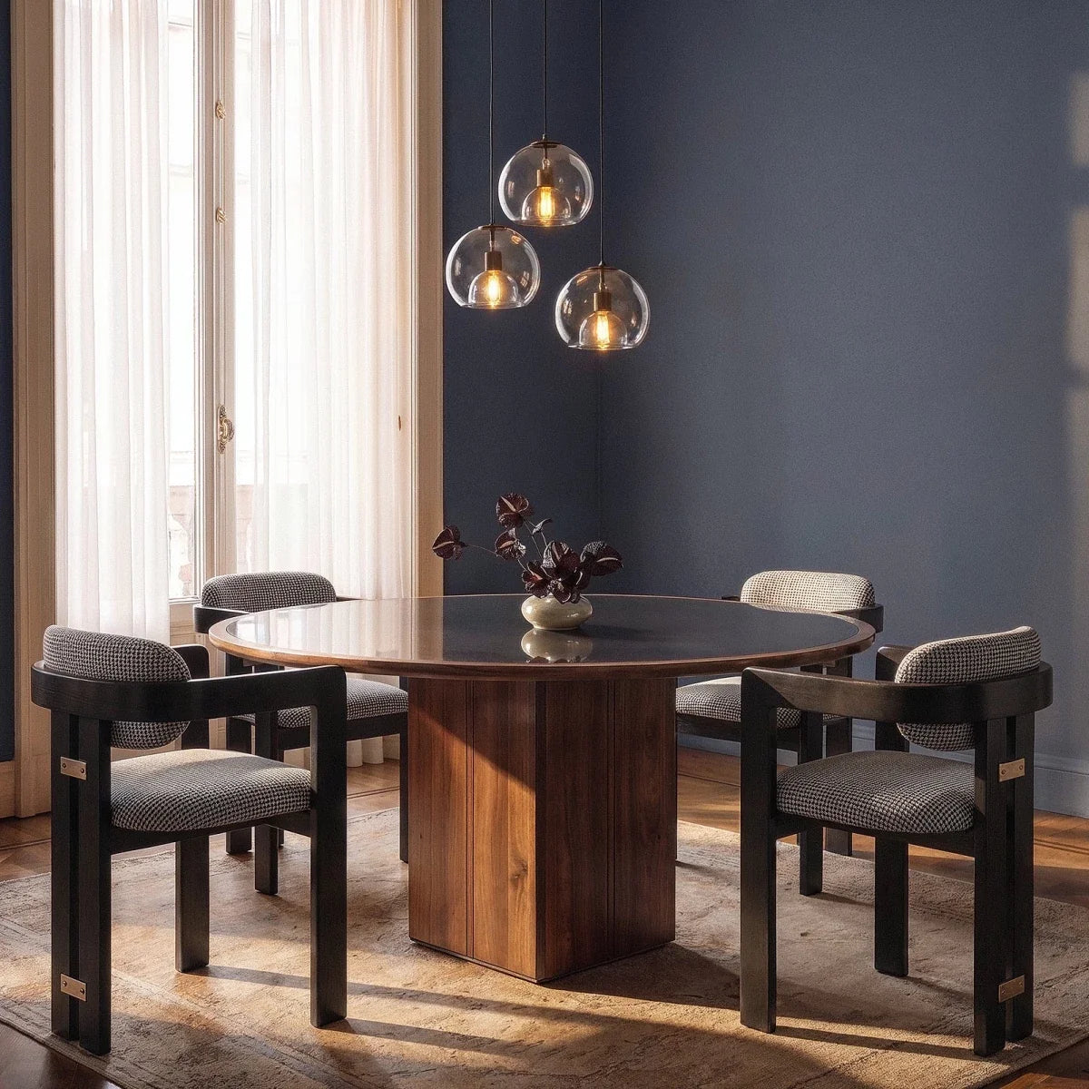 Clérachic cluster of three smoked glass pendants lit above a round walnut dining table with four houndstooth chairs.