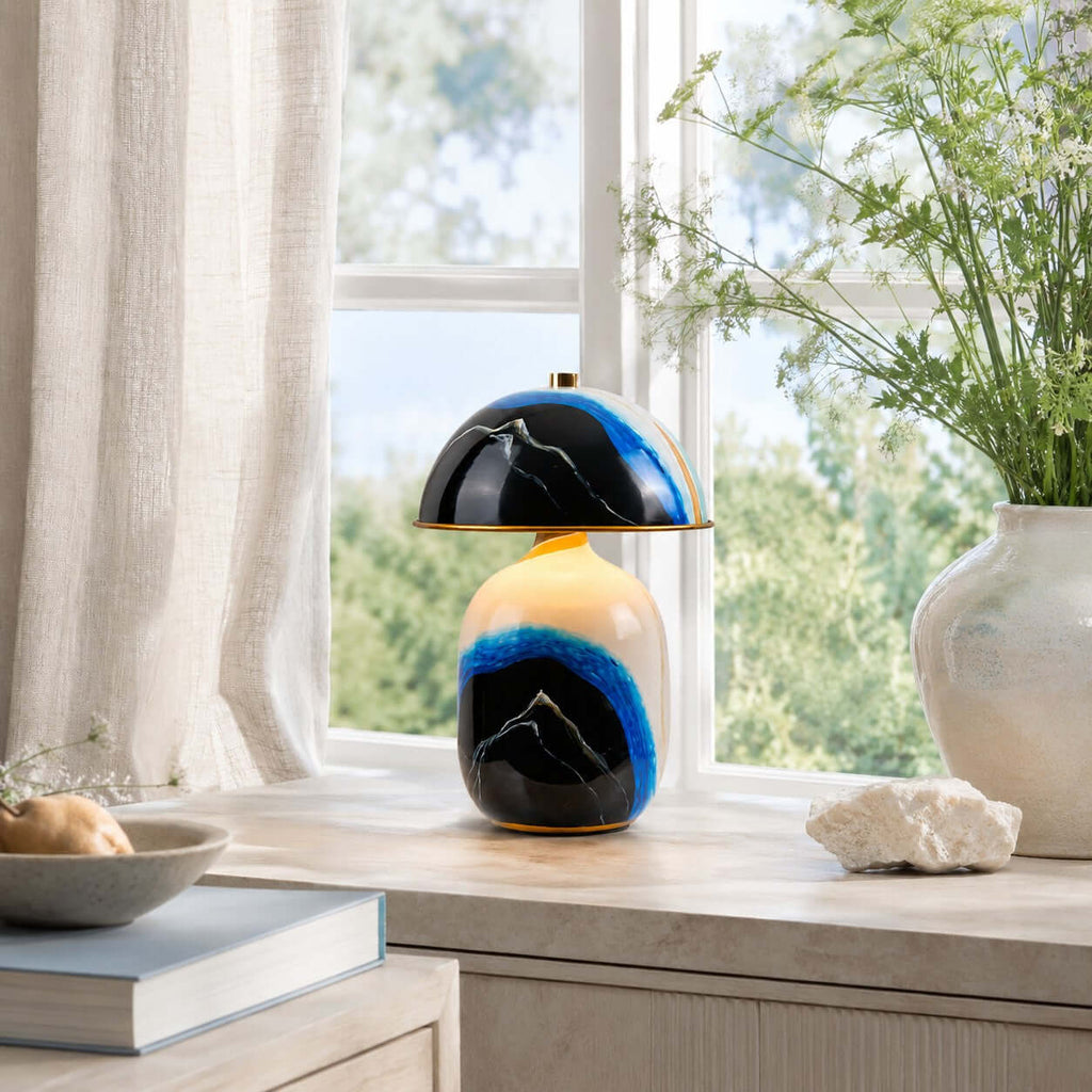 Clérachic table lamp on a window ledge in daylight, with tall white blossoms in a vase, a stone and a bowl at the front.