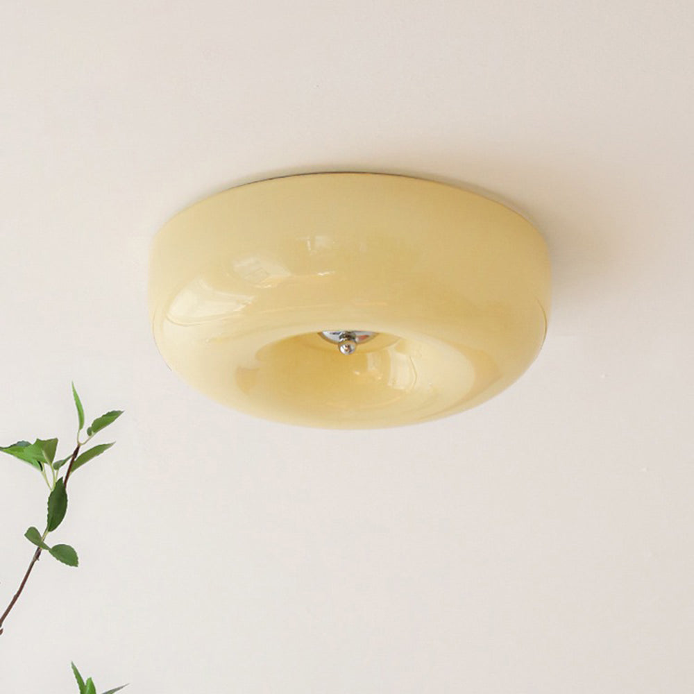 The Clérachic Domed Glass Ceiling Light seen at an angle in cream-yellow glass, a green sprig crossing the wall beneath it.