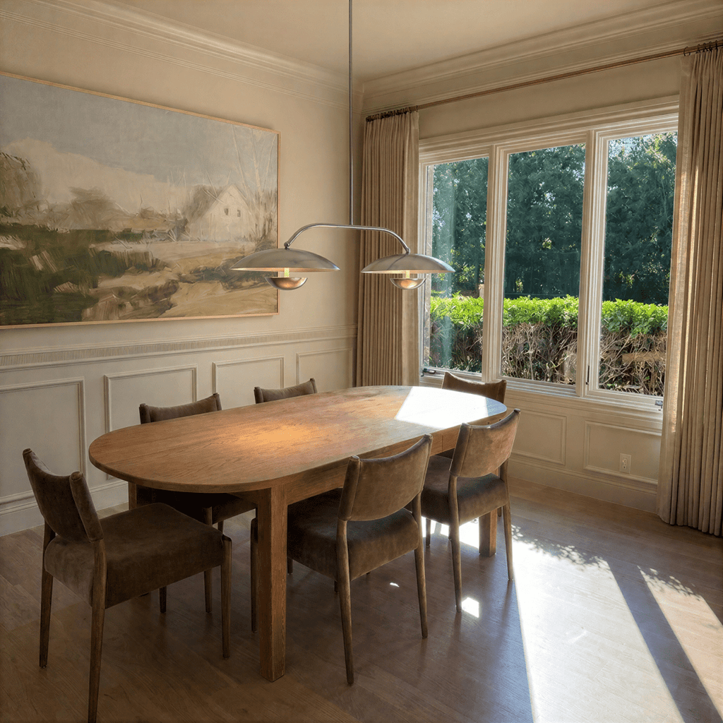 Clérachic chandelier in chrome over a dining table beneath a landscape painting and garden windows.
