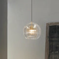 Clérachic double-wall globe pendant light in clear glass, lit against a pale plaster wall beside a framed canvas in a quiet hallway.