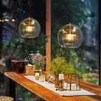 A pair of Clérachic double-wall globe pendants lighting a timber breakfast bar at dusk, the fluted inner shades glowing amber-gold.