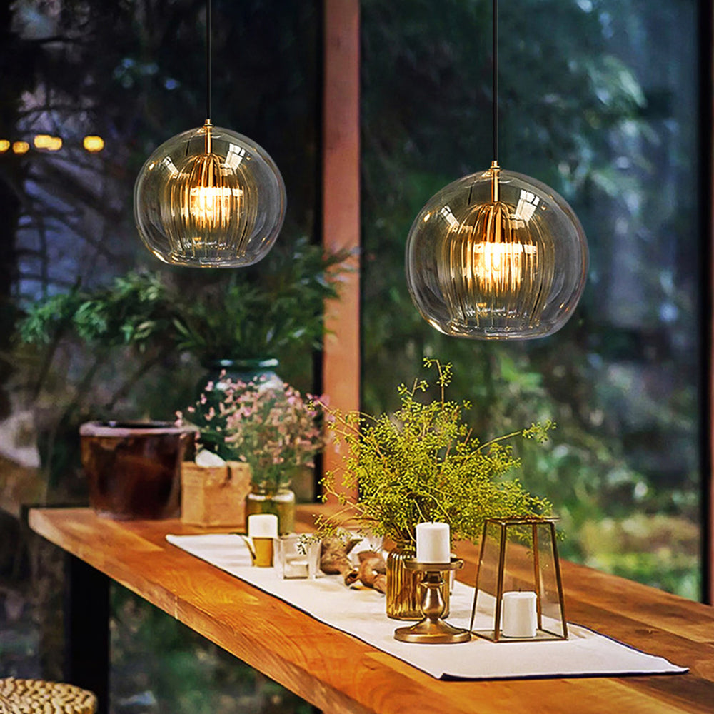 A pair of Clérachic double-wall globe pendants lighting a timber breakfast bar at dusk, the fluted inner shades glowing amber-gold.