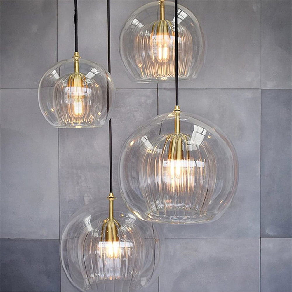 Four Clérachic double-wall globe pendants at staggered drops on a grey concrete tile wall, each ribbed inner shade lit inside its clear sphere.