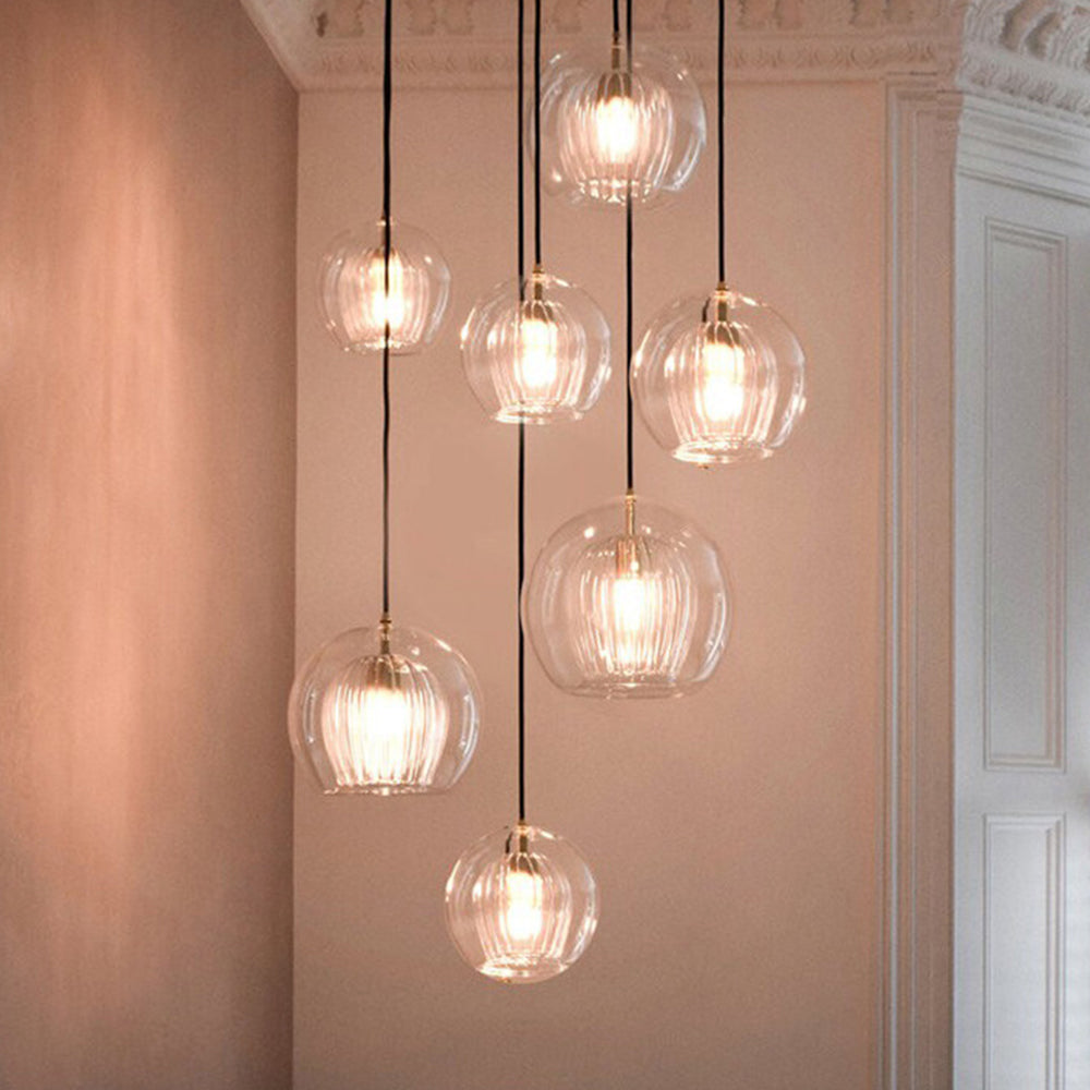 Seven Clérachic double-wall globe pendants cascading down a pink stairwell wall, hung at different heights on black braided cords.