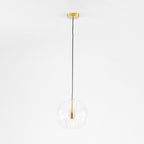 Full-drop studio shot of the Clérachic double-wall globe pendant, brushed brass canopy and long black cord above the clear globe.