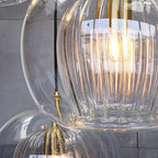 Detail of three clear Clérachic double-wall globe pendants overlapping, a lit filament seen through the fluted inner cylinder.