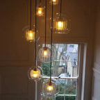 Six Clérachic double-wall globe pendants lit warm in a panelled stairwell beside a sash window at dusk.
