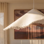 Close-up on the Clérachic pendant's raw paper-like texture and hand-frayed hem, lit warmly against framed art.