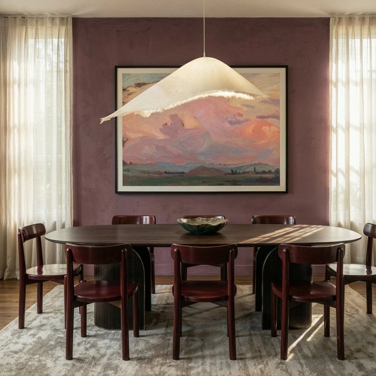 The Clérachic draped pendant hangs over a dark wood dining table, its fringed edge framed by a landscape painting.