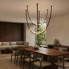 Over a long walnut dining table with a sofa behind, this Clérachic pendant hangs in a warm room, its brown straps curving into lit arcs.
