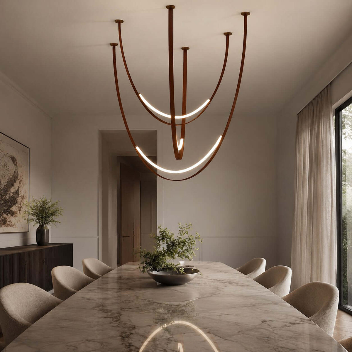 Above a long marble-topped table with cream chairs, a Clérachic pendant of brown straps shows two bright LED arcs and a reflection below.