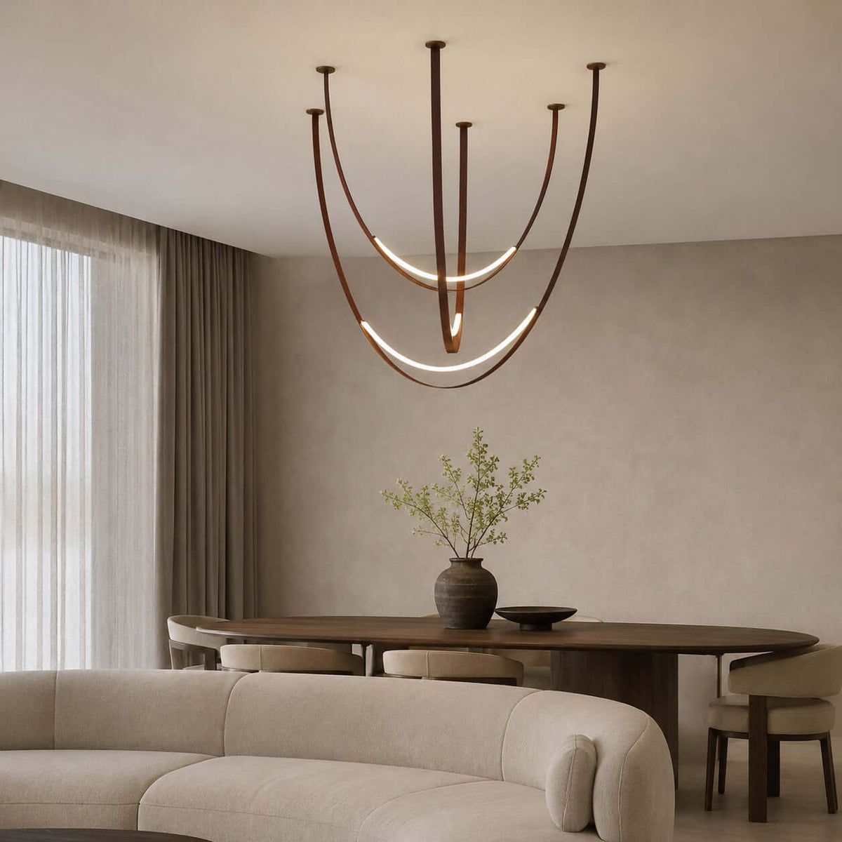 In a living and dining room with a curved cream sofa, this Clérachic pendant drapes its brown straps over a dark oval table.