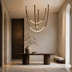 Hung in a plaster hallway with arched openings, this Clérachic pendant of brown straps glows above a dark oval console and a vase of branches.