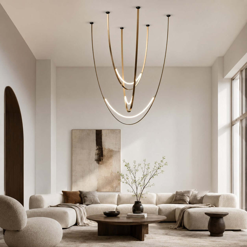 In a tall, pale living room with a low modular sofa, this Clérachic pendant hangs on brass-toned straps with glowing arcs at the bottom.