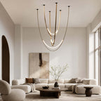 In a tall, pale living room with a low modular sofa, this Clérachic pendant hangs on brass-toned straps with glowing arcs at the bottom.