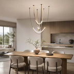 Above a wooden dining table with rounded cream chairs and a kitchen beyond, this Clérachic pendant hangs on slim brass-toned straps.