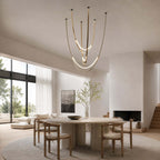 In an open room with a glazed wall and a fireplace, this Clérachic pendant on brass-toned straps hangs above a round table and wooden chairs.