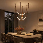 At dusk, this Clérachic pendant glows over a long wooden dining table with a vase of autumn flowers, its brown straps catching the warm light.