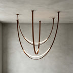 Brown-strap version of this Clérachic pendant against a grey concrete wall, its LED arcs glowing along the long, curved straps.
