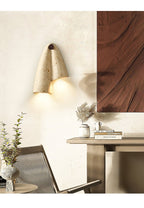 A Clérachic stone wall light glowing beside a rust-brown artwork, above a wooden console and a woven chair.