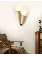 Upward-facing version of the Clérachic draped stone sconce, lit at its open top, on a cream wall beside a leather armchair.