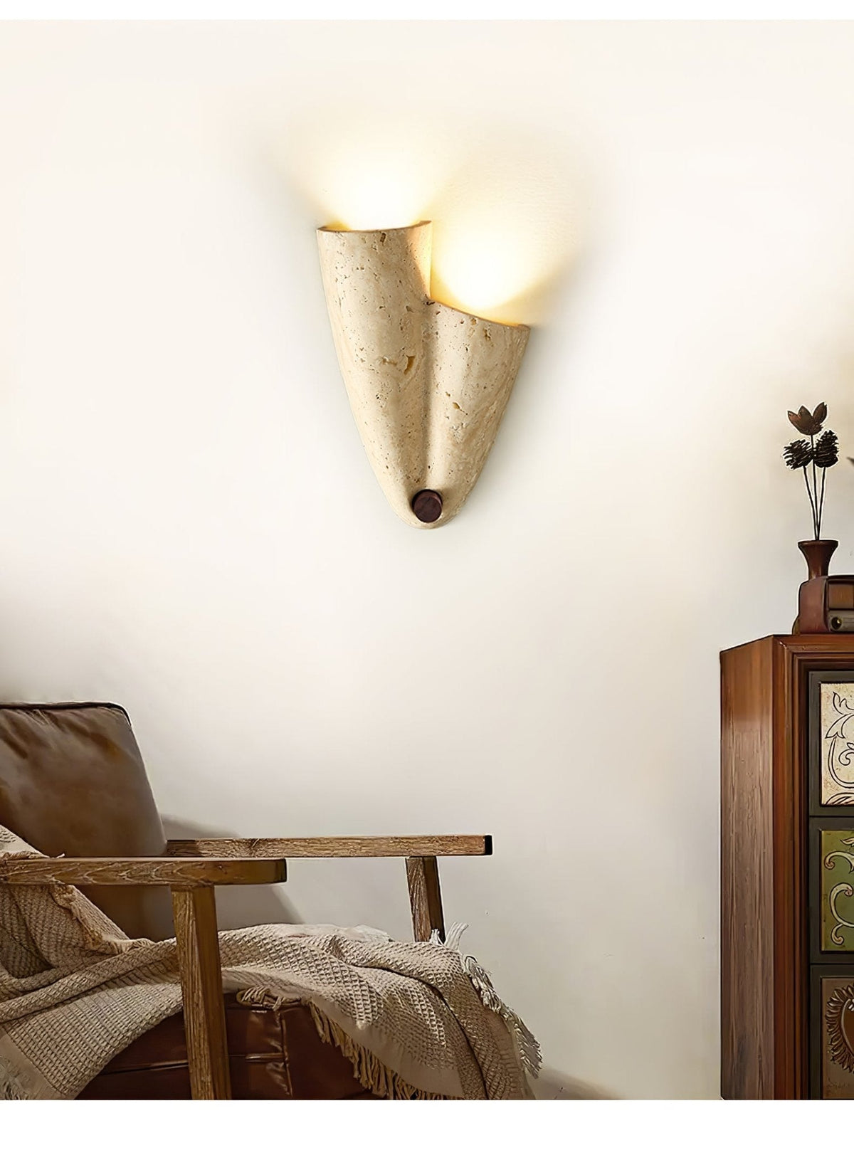 Upward-facing version of the Clérachic draped stone sconce, lit at its open top, on a cream wall beside a leather armchair.