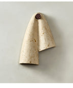 Unlit Clérachic wall sconce in pitted cream travertine, folded like a draped cloth from a round dark wood knob.