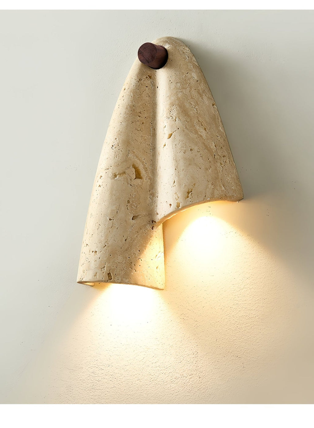 Close, lit view of the Clérachic wall light, warm light spilling from beneath the folded stone onto a pale wall.