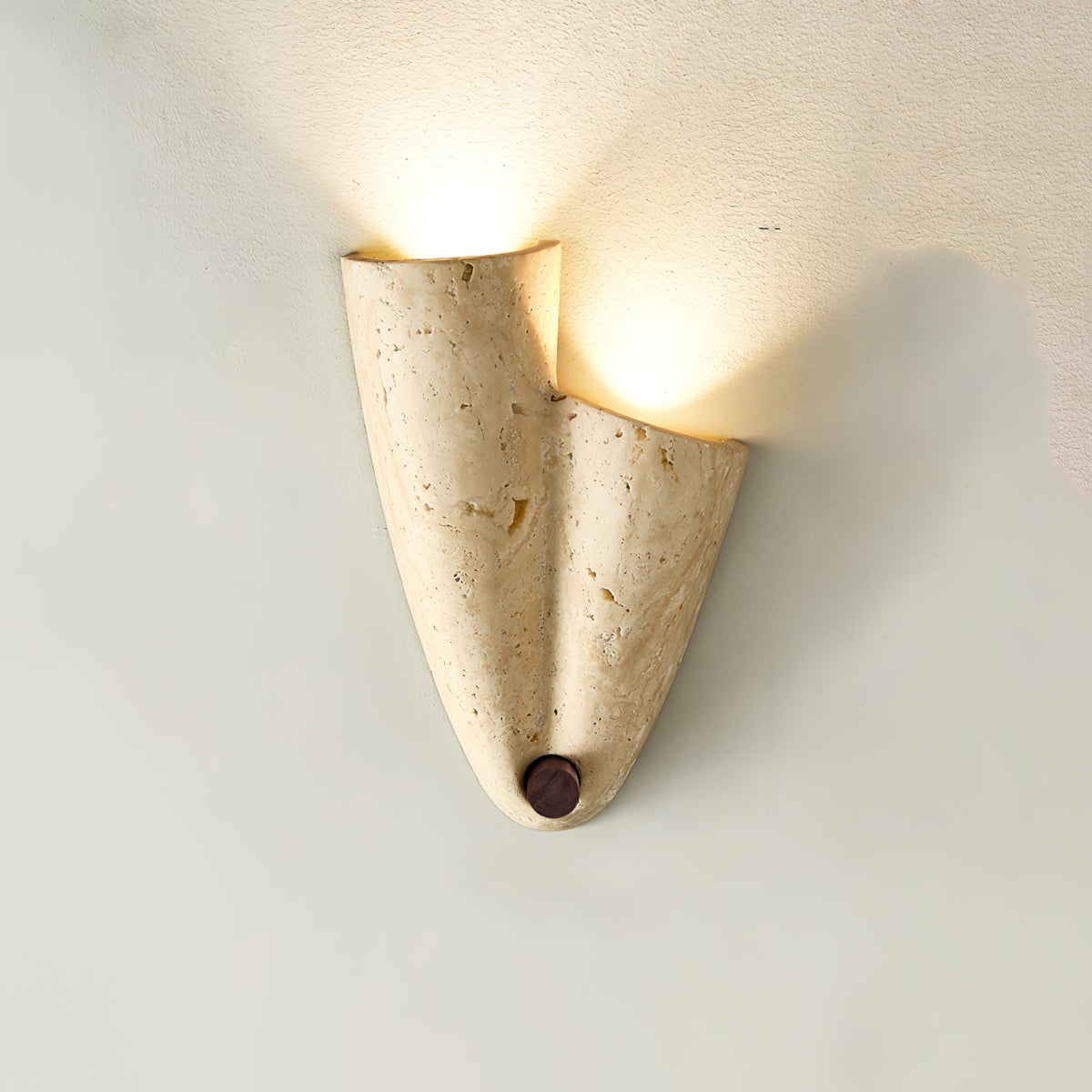 Close view of the upward version of this Clérachic sconce, light pouring from the folded top of the pitted travertine.