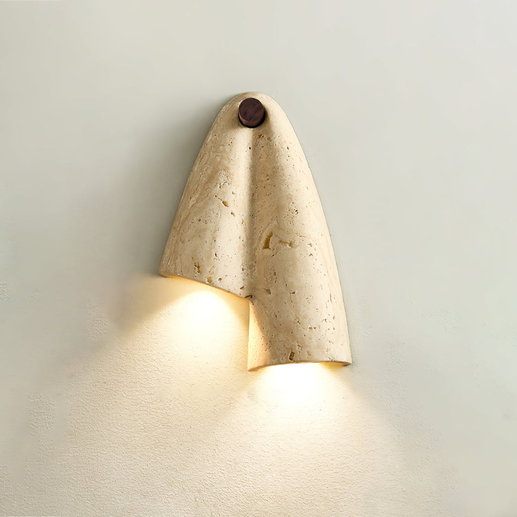 Lit Clérachic travertine wall light on a pale green-grey wall, the fold of stone sending warm light down in two pools.