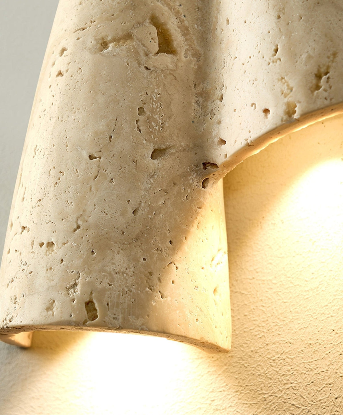 Close view of the pitted, porous travertine surface and glowing edge of the fold on this Clérachic wall light.
