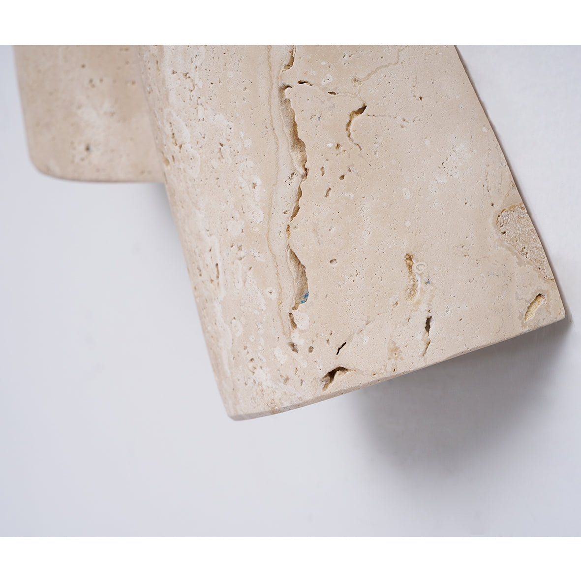Close view of the cream travertine surface of this Clérachic wall light, its natural pits and veins and a curled lower edge.