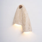 Lit Clérachic stone wall light, its fold throwing a warm pool of light below the round wood knob.