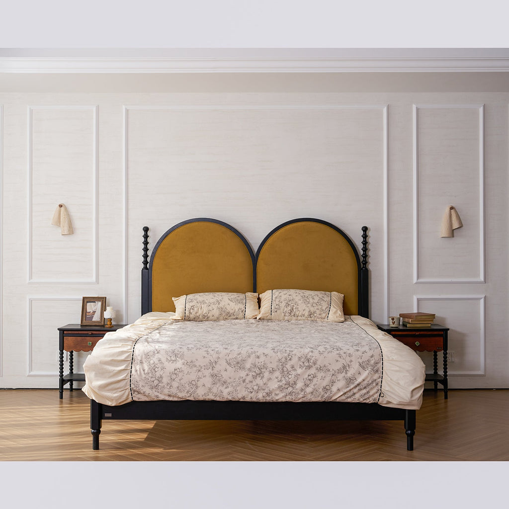 Daylight view of a bed with arched mustard headboards and a small Clérachic stone sconce on each panelled wall beside it.