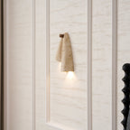 Clérachic stone wall light glowing against a travertine-effect wall with moulded panels and a black bedpost nearby.