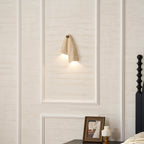 Clérachic sconce lit on a panelled wall above a framed photograph on a bedside table, seen from further back.