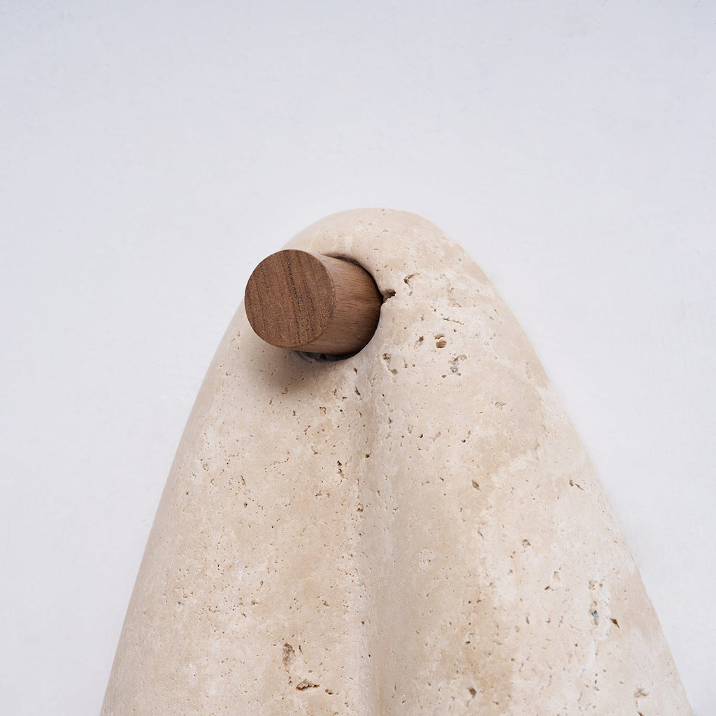 Close view of the round walnut-tone knob and the curved top of the travertine on this Clérachic wall light.