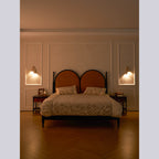 Evening bedroom with a Clérachic wall light on each side of an arched headboard, the room lit warm and the floor in herringbone wood.