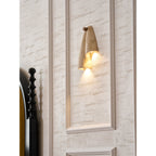 Lit Clérachic travertine wall light on a moulded panel, with a black bedpost and a mustard headboard at the left.