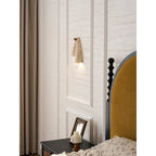 Tall view of a Clérachic stone wall light on a panelled wall, beside a curtain, a framed photo and a mustard headboard.